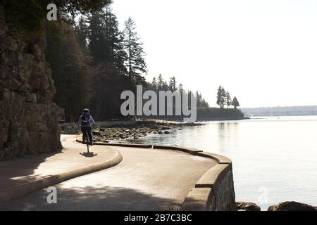 Vancouver, Canada - 21 febbraio 2020: Una donna sta cavalcando sul sentiero del muro di mare vicino alla terza spiaggia nello Stanley Park durante la bella giornata di sole Foto Stock