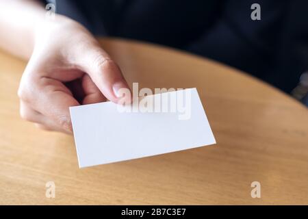 Donna d'affari che tiene e che dà un biglietto da visita vuoto a qualcuno sul tavolo in ufficio Foto Stock