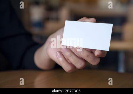 Mano della donna che tiene e mostra un biglietto da visita vuoto sul tavolo in ufficio Foto Stock
