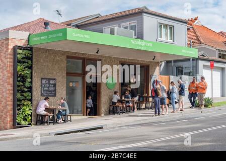 La gente aspetta e mangia al di fuori della Wholegreen Bakery a Sydney, Australia, sobborgo di Waverly. Wholegreen è un panettiere completamente privo di glutine e fornitore. Foto Stock