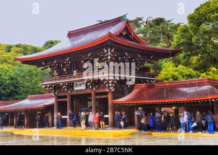 Tokyo, Giappone - 31 dicembre 2020: Il giardino imperiale e il complesso del tempio di Buiddhism Meiji-jingu. Ingresso cancello intorno cortile interno sotto la pioggia con hidi turisti Foto Stock