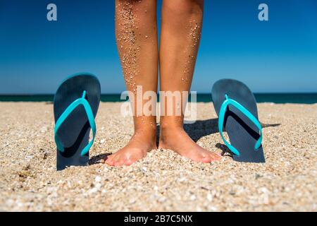 infradito blu e gambe umane sulla sabbia - un concetto per vacanze estive, viaggi e tempo libero - focus selettivo, spazio copia Foto Stock