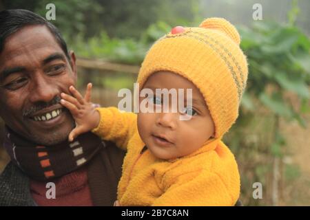 Un bambino del Bangladesh che indossa un maglione giallo paga con il padre durante l'inverno a Sirajgonj , Bangladesh Foto Stock