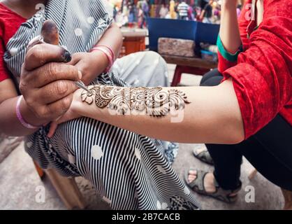 Donna indiana che fa pittura di hennè sulla mano turistica alla strada principale del bazar a Delhi Foto Stock