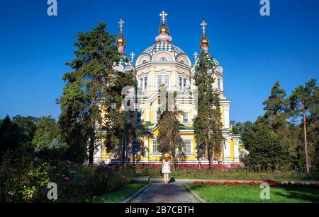 Donna in abito bianco e cappello giallo che guarda alla famosa chiesa ortodossa di Almaty, Kazakhstan Foto Stock