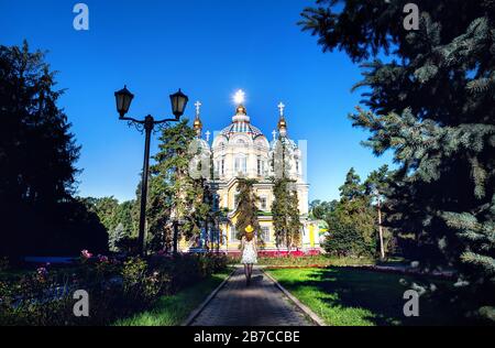 Donna in abito bianco e cappello giallo che guarda alla famosa chiesa ortodossa di Almaty, Kazakhstan Foto Stock