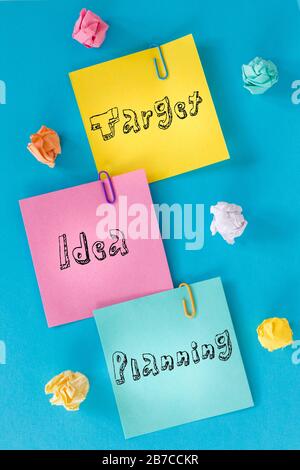 Carte colorate con iscrizioni 'obiettivo, idea, pianificazione' palle di carta sbriciolate, punti metallici per ufficio, concetto di pianificazione e motivazione nel business Foto Stock