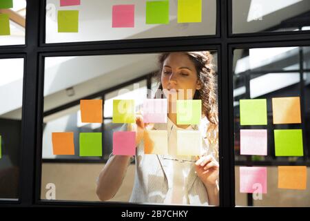 Attività di scrittura focalizzate di businesswoman su adesivi su tavola di vetro Foto Stock