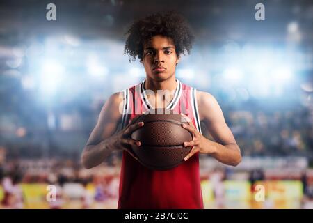 Il giocatore di pallacanestro tiene la palla nel cestino dello stadio pieno di spettatori. Foto Stock