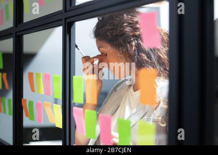 Stanco uomo d'affari che tocca il ponte nasale, lavorando con carte appiccicose Foto Stock