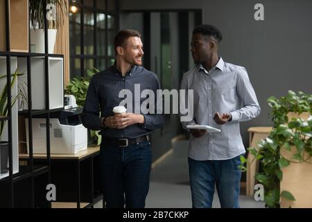 Sorridendo diversi colleghi che parlano, camminando in un ufficio moderno Foto Stock
