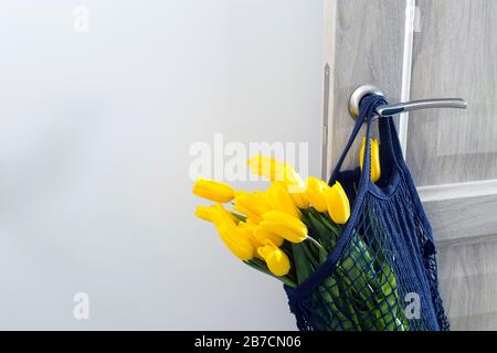 Tulipani gialli in una borsa a tracolla blu marino ecologica appesa su una porta beige. Foto Stock