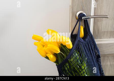 Tulipani gialli in una borsa a tracolla blu marino ecologica appesa su una porta beige. Foto Stock