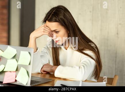 Concetto freelance multitasking. La ragazza stanca tiene la testa Foto Stock