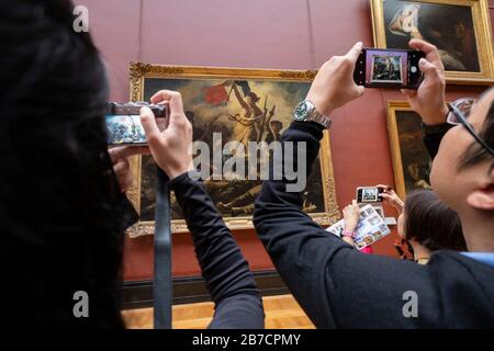 Tre turisti che scattano foto della libertà che guida la gente dipingendo dall'artista Eugene Delacroix al Museo del Louvre di Parigi, Francia, Europa Foto Stock