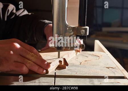 primo piano delle mani di un operatore che sega tavole di legno su una sega a nastro. Foto Stock