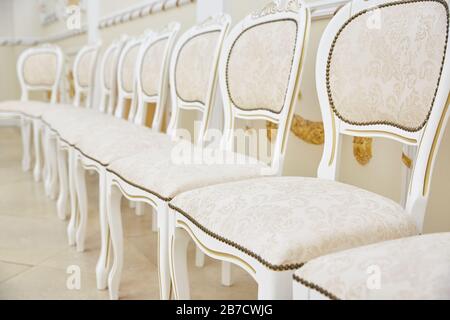 Una fila di sedie bianche dal design classico in una stanza luminosa. Seduta e schienale straccio. Nessuno Foto Stock