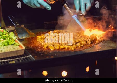 Uomo che frittura maiale da fiamma di fuoco sulla stufa a Street Night Market. Foto Stock