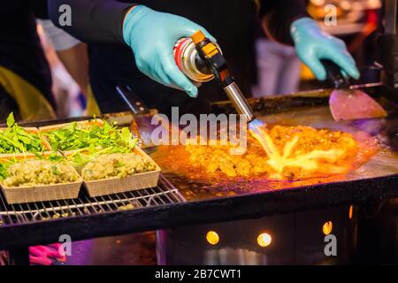 Uomo che frittura maiale da fiamma di fuoco sulla stufa a Street Night Market. Foto Stock