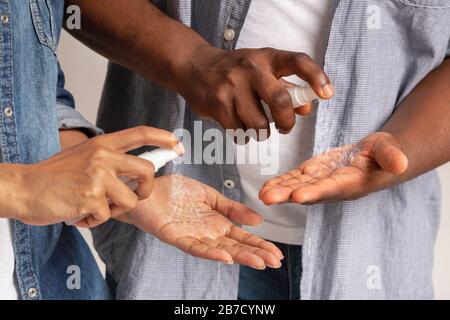 Uomo e donna nero irriconoscibile applicazione di spray disinfettante sulle mani, Closeup Foto Stock