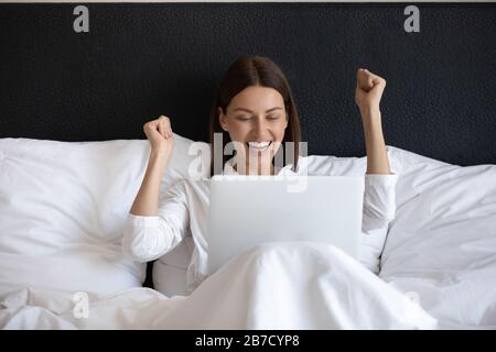 Giovane donna entusiasta che guarda lo schermo del notebook, che si rilassa a letto. Foto Stock