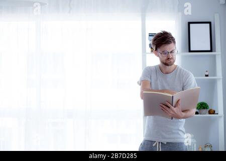 Bel ragazzo in occhiali è la lettura di libro preparazione esame con permanente al soggiorno - concetto di istruzione. Foto Stock
