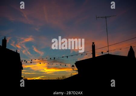 Silhouette di case al tramonto in un villaggio con nuvole arancioni Foto Stock