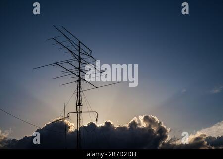 Sunbeams tra le nuvole nel cielo blu sopra un'antenna Foto Stock