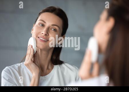 Pelle detergente giovane donna, viso esfoliante con spugna. Foto Stock