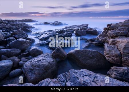 Una fotografia pre-alba di onde nebbie che si schiantano sulle rocce dalla costa meridionale in Sudafrica Foto Stock