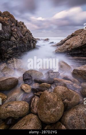 Una fotografia di paesaggio al tramonto verticale di onde nebbie che si schiantano sulle rocce dalla costa meridionale in Sudafrica Foto Stock