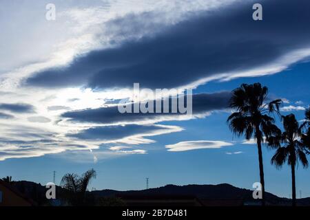 Silhouette di torri ad alta tensione e palme su blu cielo con nuvole bianche Foto Stock