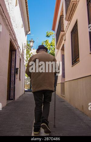 Vecchio uomo che cammina lungo la strada con un crutch in una strada della città Foto Stock