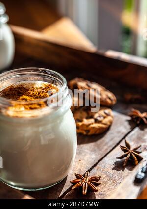 Primo piano di una tazza di Sahlep turco caldo su una superficie rustica con bastoncini di cannella e biscotti Foto Stock