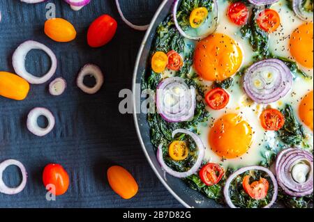 Primo piano di una frittata con spinaci in una padella e decorata con cipolla fresca, pomodori e spinaci Foto Stock