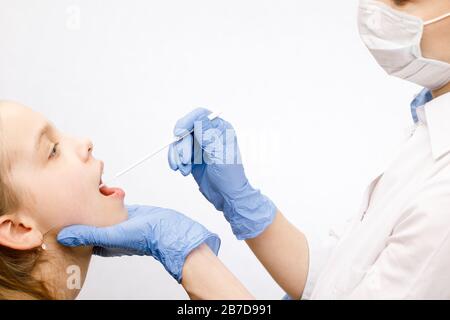 Pediatra o medico che preleva il campione di saliva dalla bocca della ragazza di età elementare eseguendo la procedura diagnostica di analisi della saliva (Salivaomics) Foto Stock