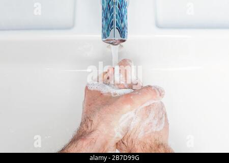 Uomo lavando le mani con sapone antibatterico e acqua che attuano le misure protettive di base contro la diffusione dell'epidermide del coronavirus Foto Stock