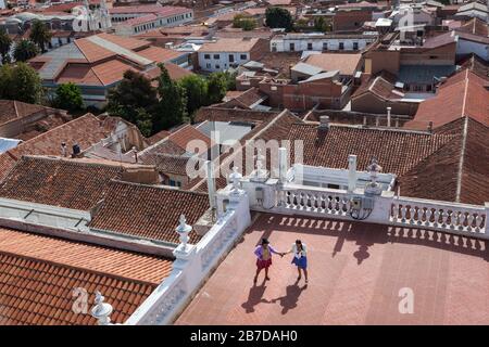 Sucre, Bolivia: Due ragazze indigene boliviane in abiti tradizionali su tetto di mattoni rossi. Strade coloniali della capitale boliviana Foto Stock