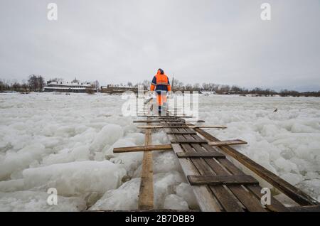 Un uomo cammina sulle tavole attraverso una traversata di ghiaccio. Attraversando un fiume ghiacciato. Russia, Arkhangelsk Foto Stock