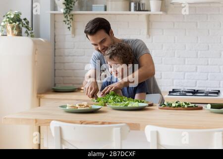 Il padre che si prende cura di lui insegna al figlio piccolo a tritare le verdure Foto Stock