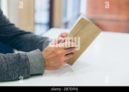 Giovane uomo che legge il vecchio libro di carta aperto al tavolo, primo piano, stile vintage Foto Stock