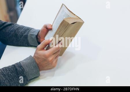 Giovane uomo che legge il vecchio libro di carta aperto al tavolo, primo piano, stile vintage Foto Stock