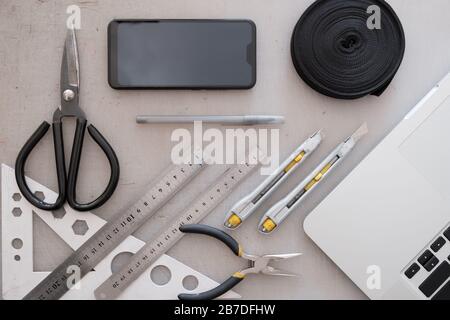 Area di lavoro di progettazione tecnica o industriale, vista dall'alto. Piatto con computer portatile, smartphone, corda, forbici, righelli e coltelli con grunge posteriore Foto Stock