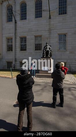 Massachusetts, Stati Uniti. 14 Marzo 2020. I visitatori scattano foto con la scultura del fondatore dell'Università di Harvard John Harvard nel Harvard Yard, centro del campus di Harvard, il viso di Harvard è stato coperto da una maschera facciale. In reazione a Coronavirus preoccupazioni Harvard University ha annunciato che a partire dal 23 marzo 2020 tutte le classi saranno remote o online. Agli studenti che vivono nelle residenze universitarie è stato chiesto di partire entro marzo 22 2020. Credit: Chuck Nacke/Alamy Live News Foto Stock