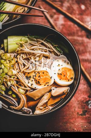 Zuppa tradizionale giapponese Ramen con carne di pollo e funghi shiitake in ciotole nere e bacchette di bambù su sfondo tavolo rosso scuro, t Foto Stock