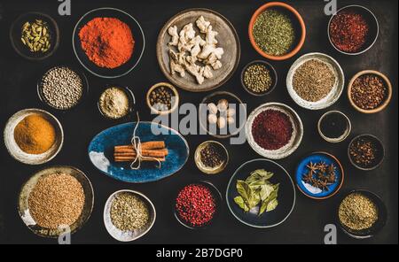 Piatto di spezie in ciotole e piatti su sfondo scuro, vista dall'alto. Pepe nero, allspezia, chiodi di garofano, timo, cumino, sesamo, anice stellato, zenzero, cinna Foto Stock