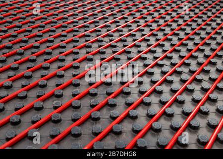 Impianto di riscaldamento a pavimento radiante con tubo flessibile rosso montato su pannelli isolanti neri Foto Stock