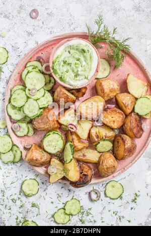 Insalata di patate arrosto con cetrioli, aneto e yogurt condimento, servito su piatto rosa e sfondo grigio. Foto Stock