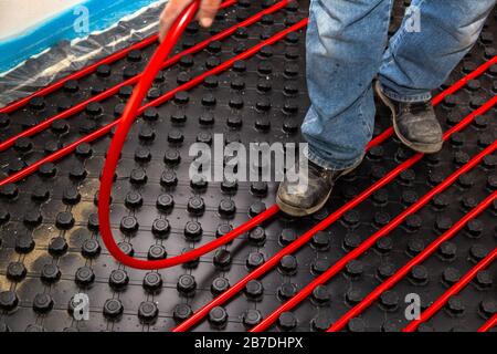 Lavoratore che installa tubi rossi di impianto di riscaldamento a pavimento radiante Foto Stock