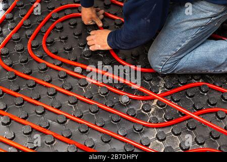 Lavoratore che installa tubi di impianto di riscaldamento a pavimento radiante Foto Stock